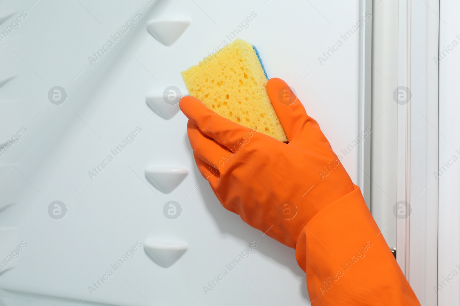 Photo of Worker in rubber gloves cleaning empty refrigerator, closeup