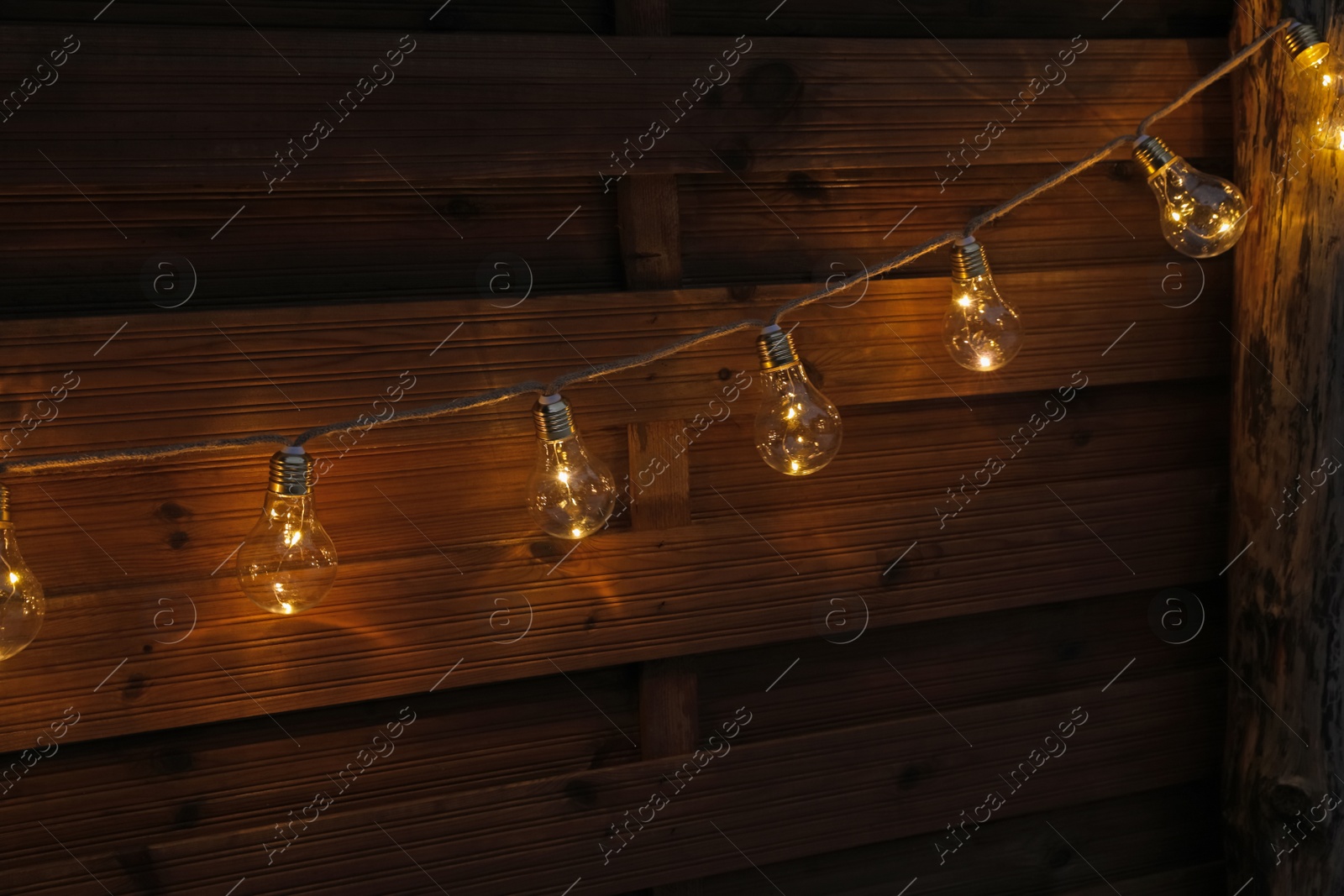 Photo of Garland of lamp bulbs hanging on wooden wall. String lights