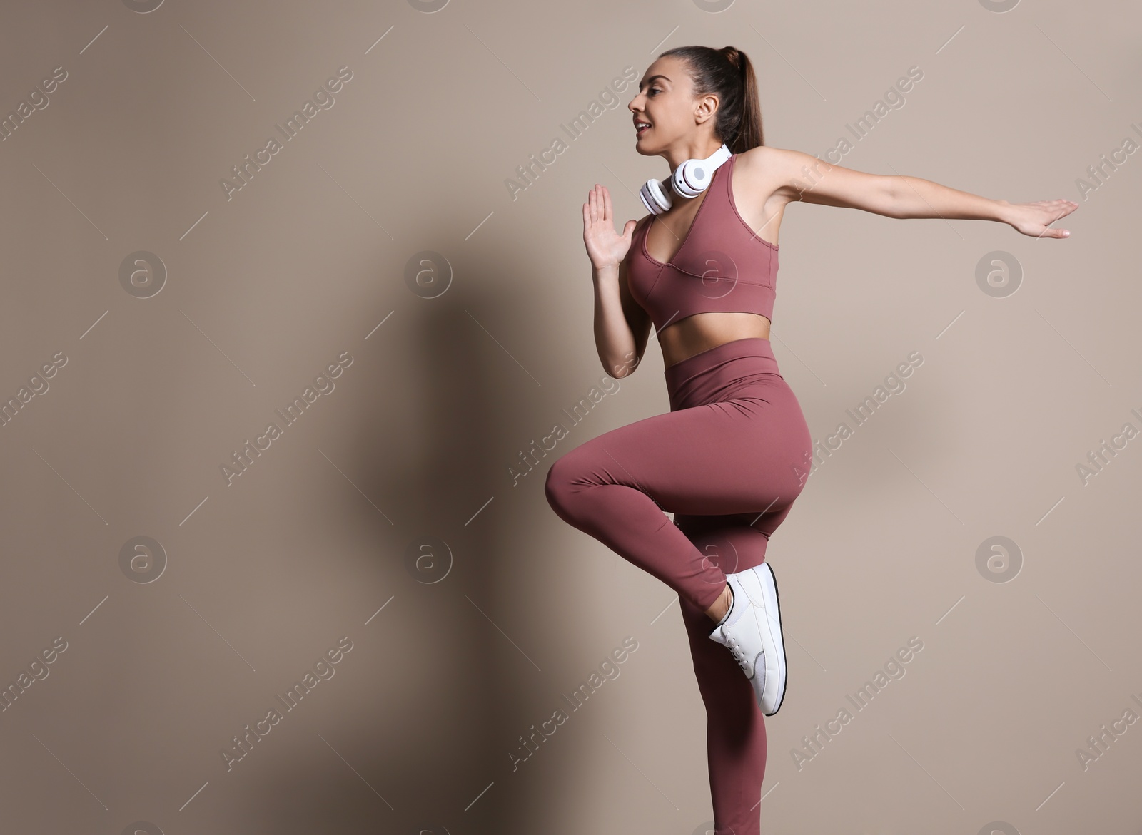 Photo of Young woman in sportswear with headphones running on beige background. Space for text