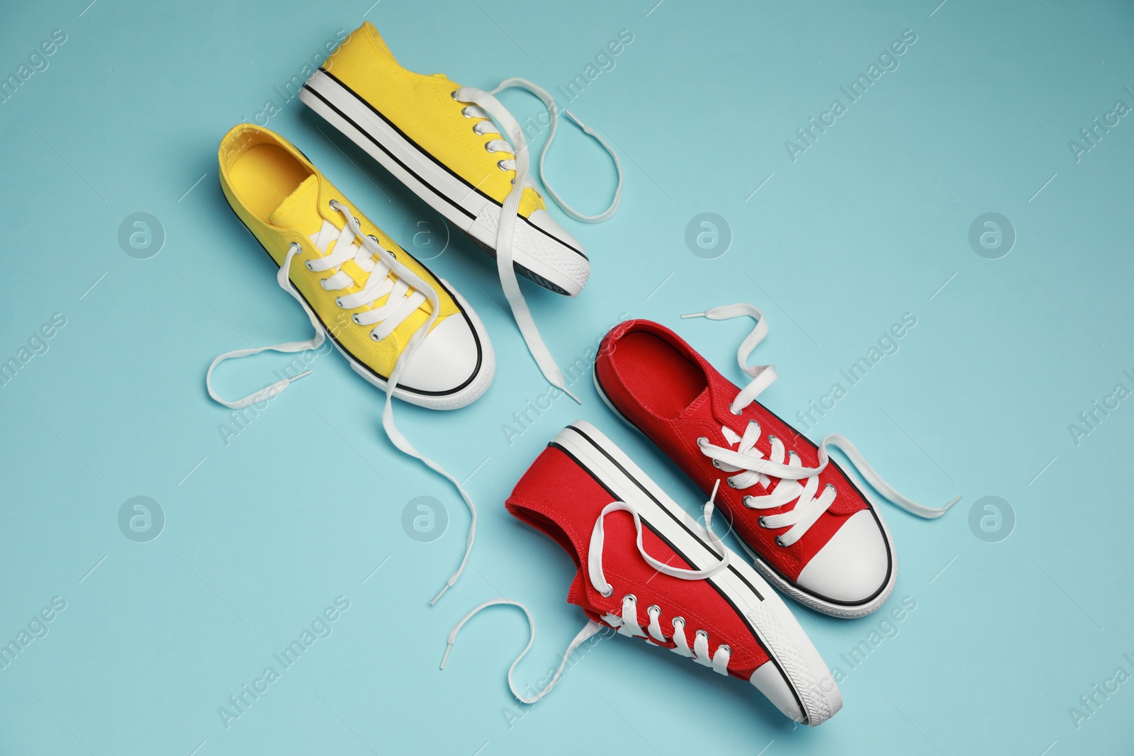 Photo of Red and yellow classic old school sneakers on light blue background, flat lay