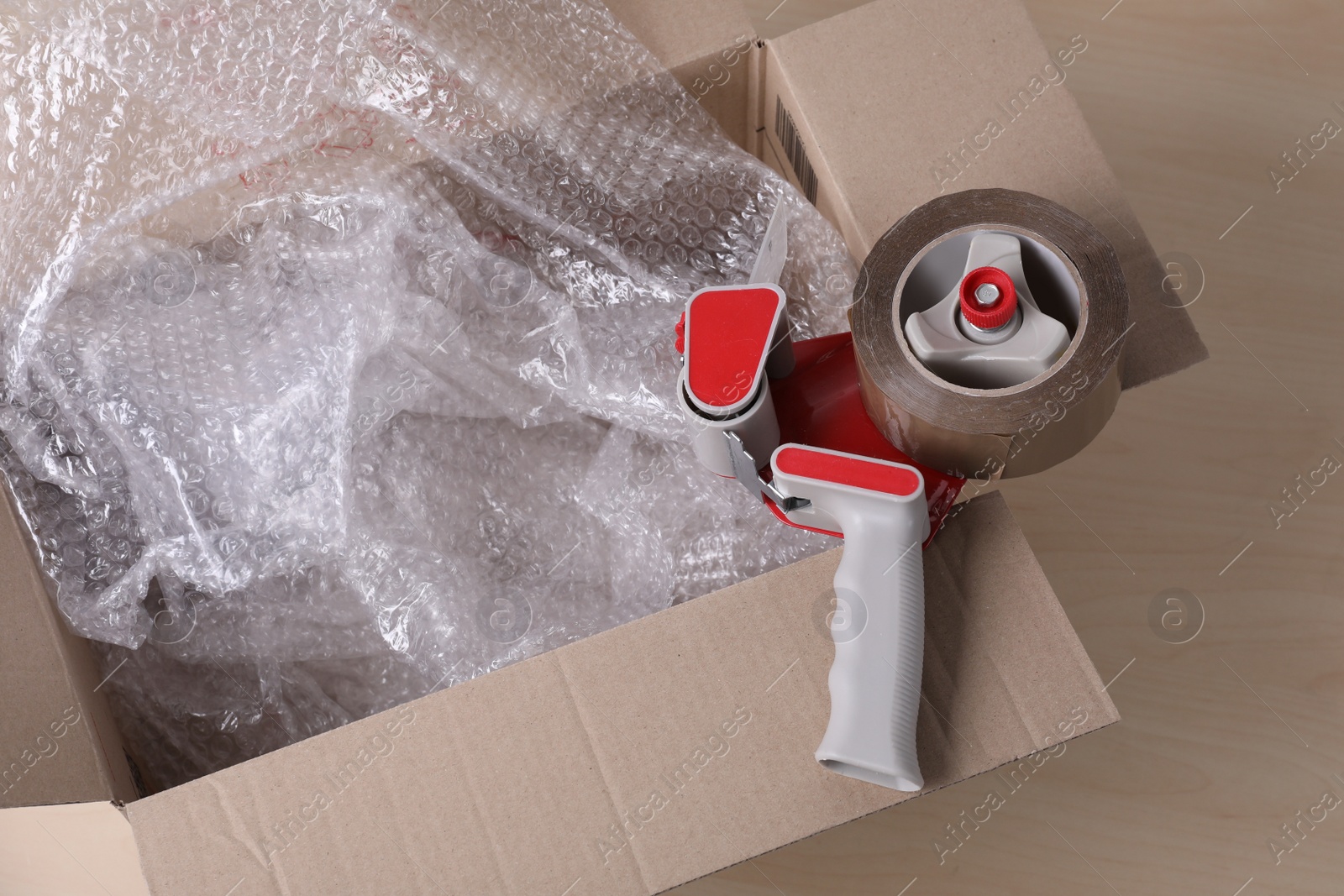 Photo of Cardboard box with bubble wrap and adhesive tape on wooden table