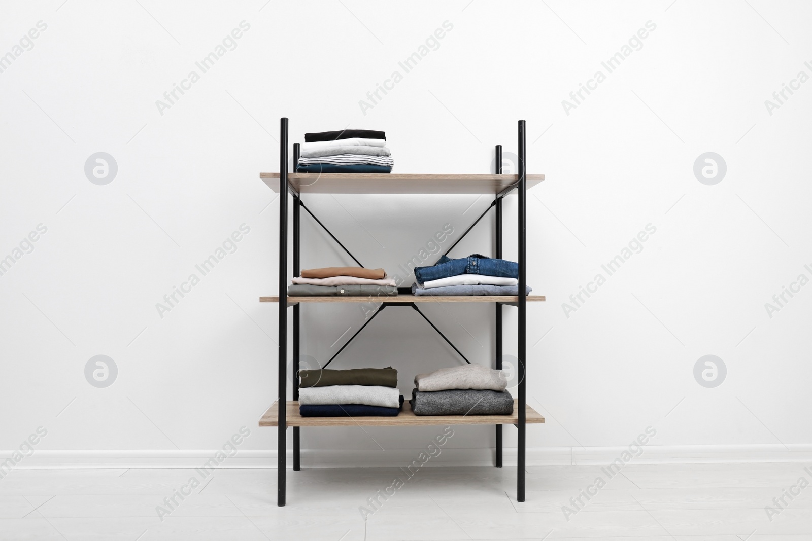 Photo of Modern shelves unit with stacked clothes near white wall