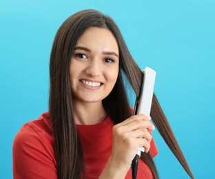 Young woman using hair iron on blue background, space for text