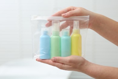 Photo of Woman holding plastic bag of cosmetic travel kit indoors, closeup. Bath accessories
