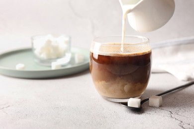 Photo of Pouring milk into cup with coffee on white textured table, closeup