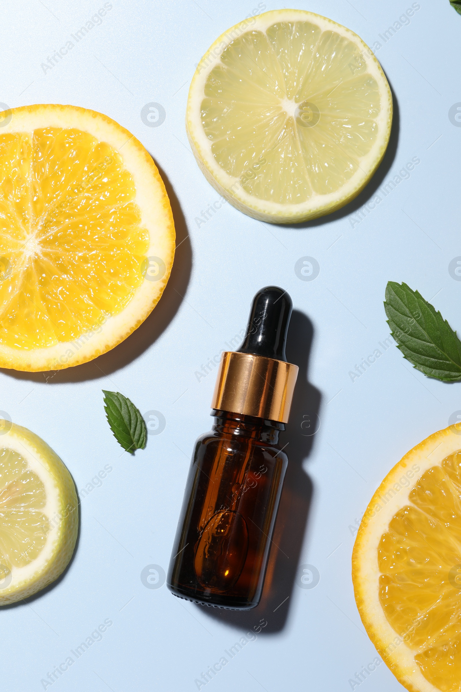 Photo of Bottle of cosmetic serum, sliced citrus fruits and green leaves on light blue background, flat lay