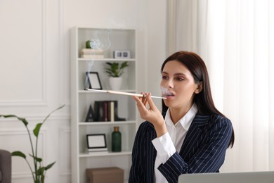 Woman using long cigarette holder for smoking at workplace in office
