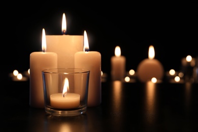 Burning candles on table in darkness, space for text. Funeral symbol