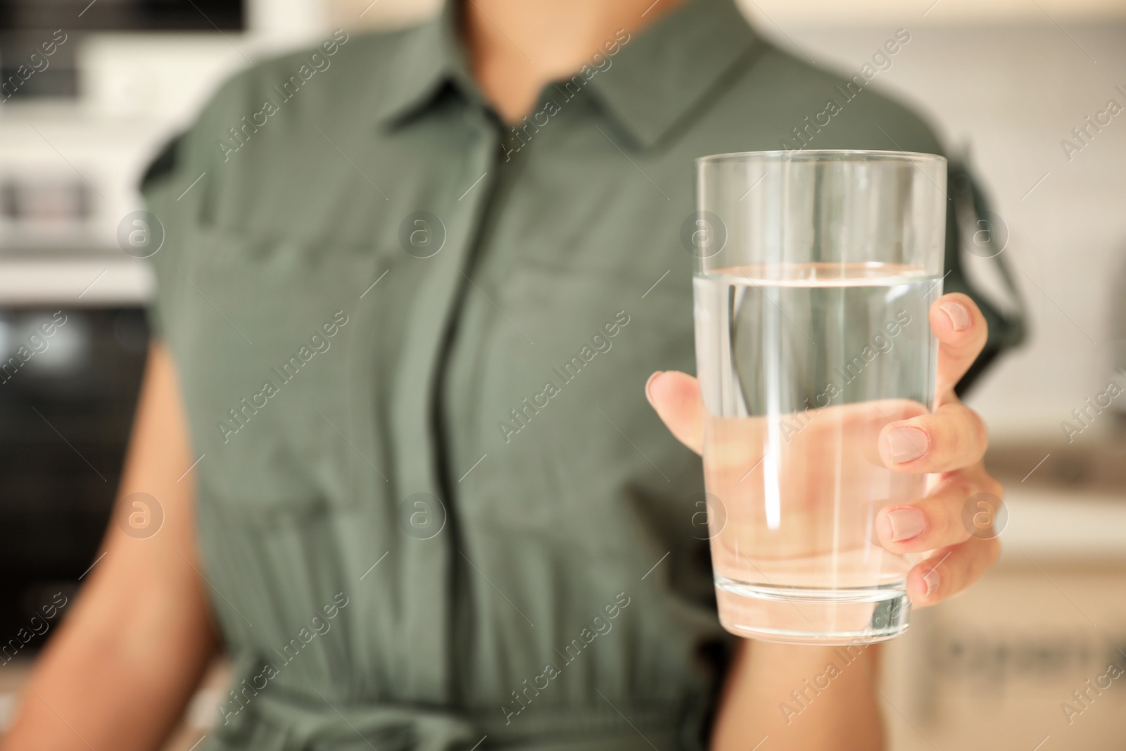 Photo of Woman holding glass with pure water in kitchen, closeup