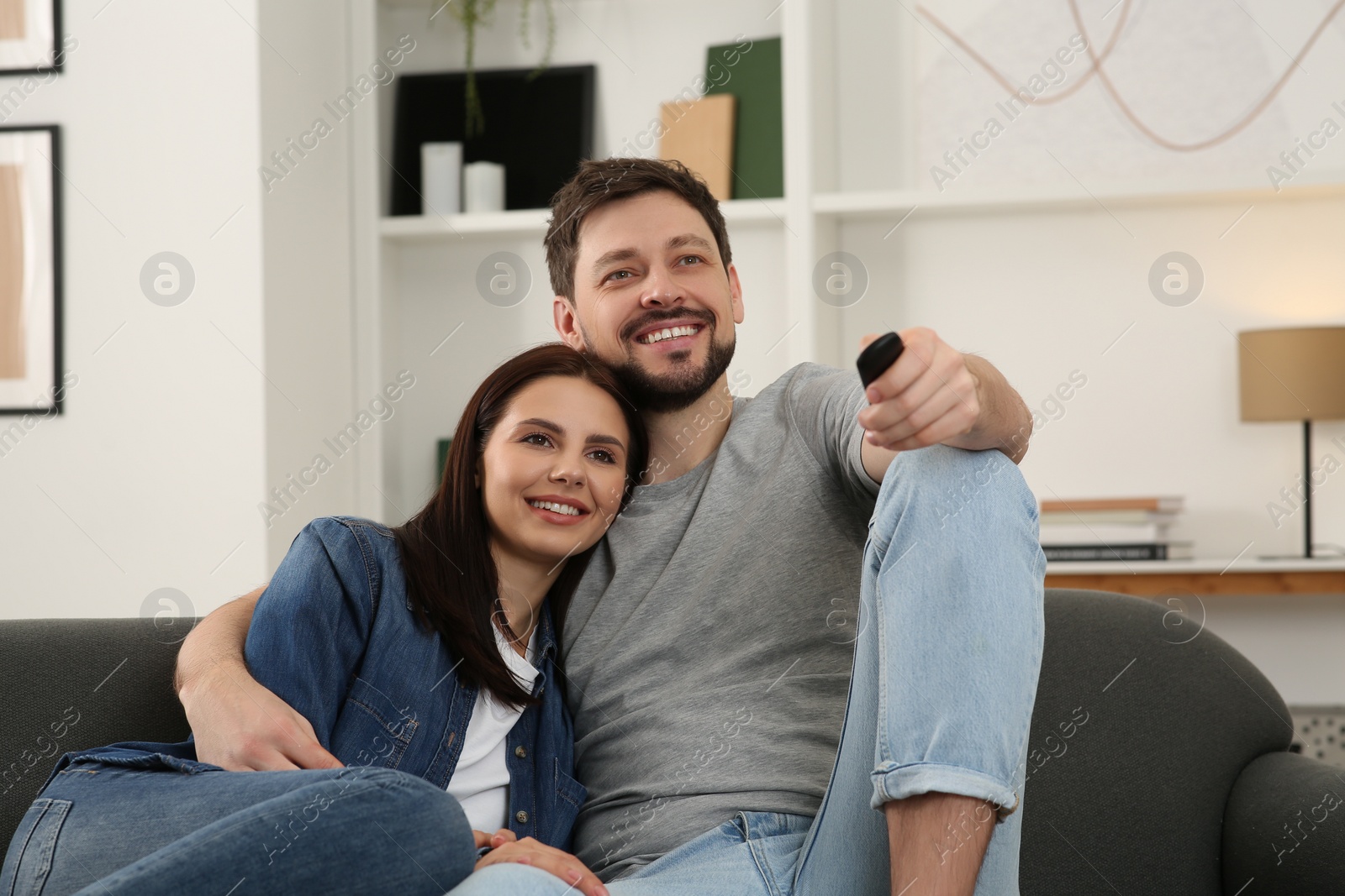 Photo of Happy couple watching show at home. Man changing TV channels with remote control