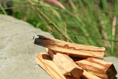 Smoldering palo santo sticks on stone outdoors, closeup. Space for text