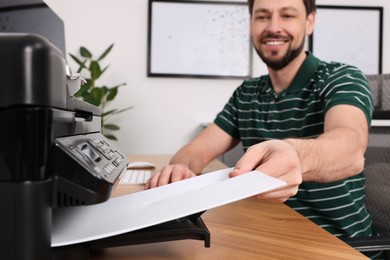 Photo of Man using modern printer at wooden table indoors, selective focus