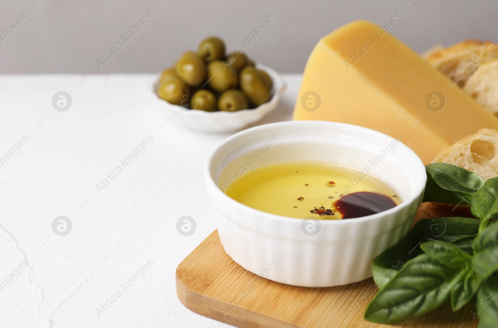 Photo of Bowl of organic balsamic vinegar with oil, basil, bread and cheese on white table, space for text