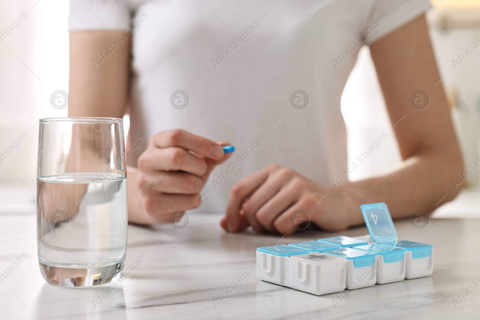 Photo of Woman with pills, organizer and glass of water at white marble table, closeup