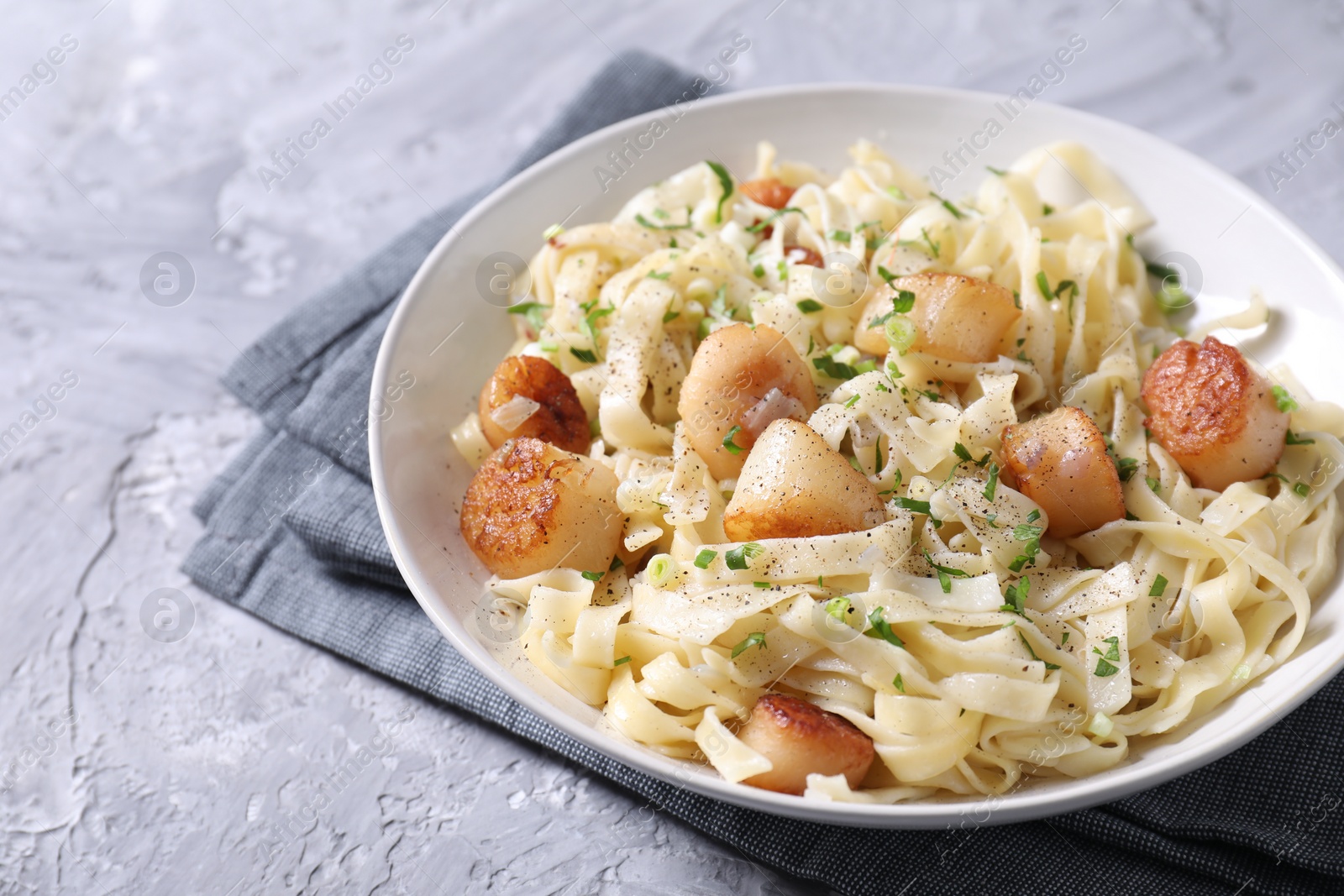 Photo of Delicious scallop pasta with spices in bowl on gray textured table, closeup