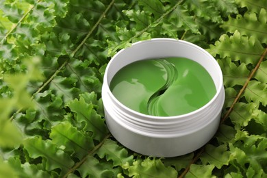 Photo of Jar of under eye patches on green fern leaves, closeup. Cosmetic product