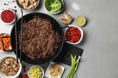 Wok with noodles, chicken and other products on light grey table, flat lay. Space for text