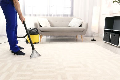 Man removing dirt from carpet with vacuum cleaner indoors, closeup. Space for text