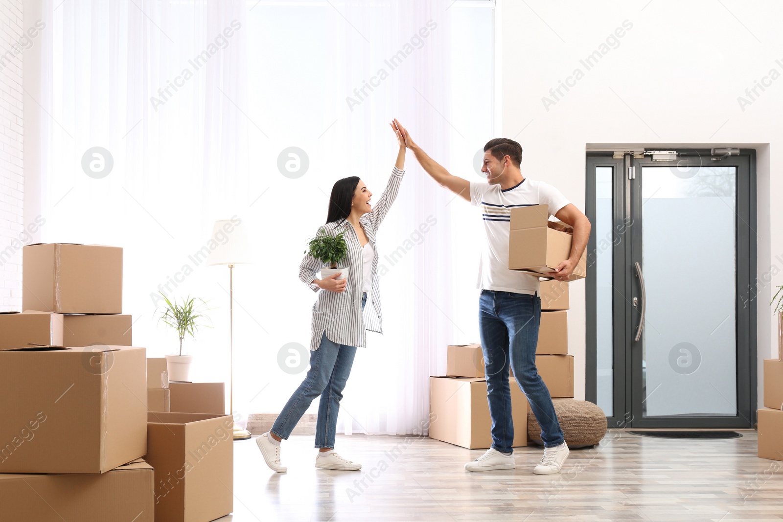 Photo of Happy couple in room with cardboard boxes on moving day