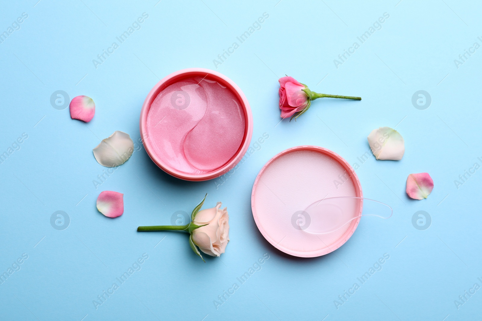 Photo of Under eye patches in jar and rose flowers on light blue background, flat lay. Cosmetic product