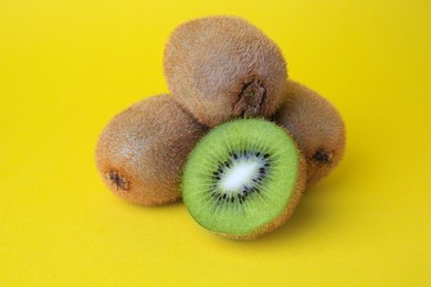 Heap of whole and cut fresh kiwis on yellow background