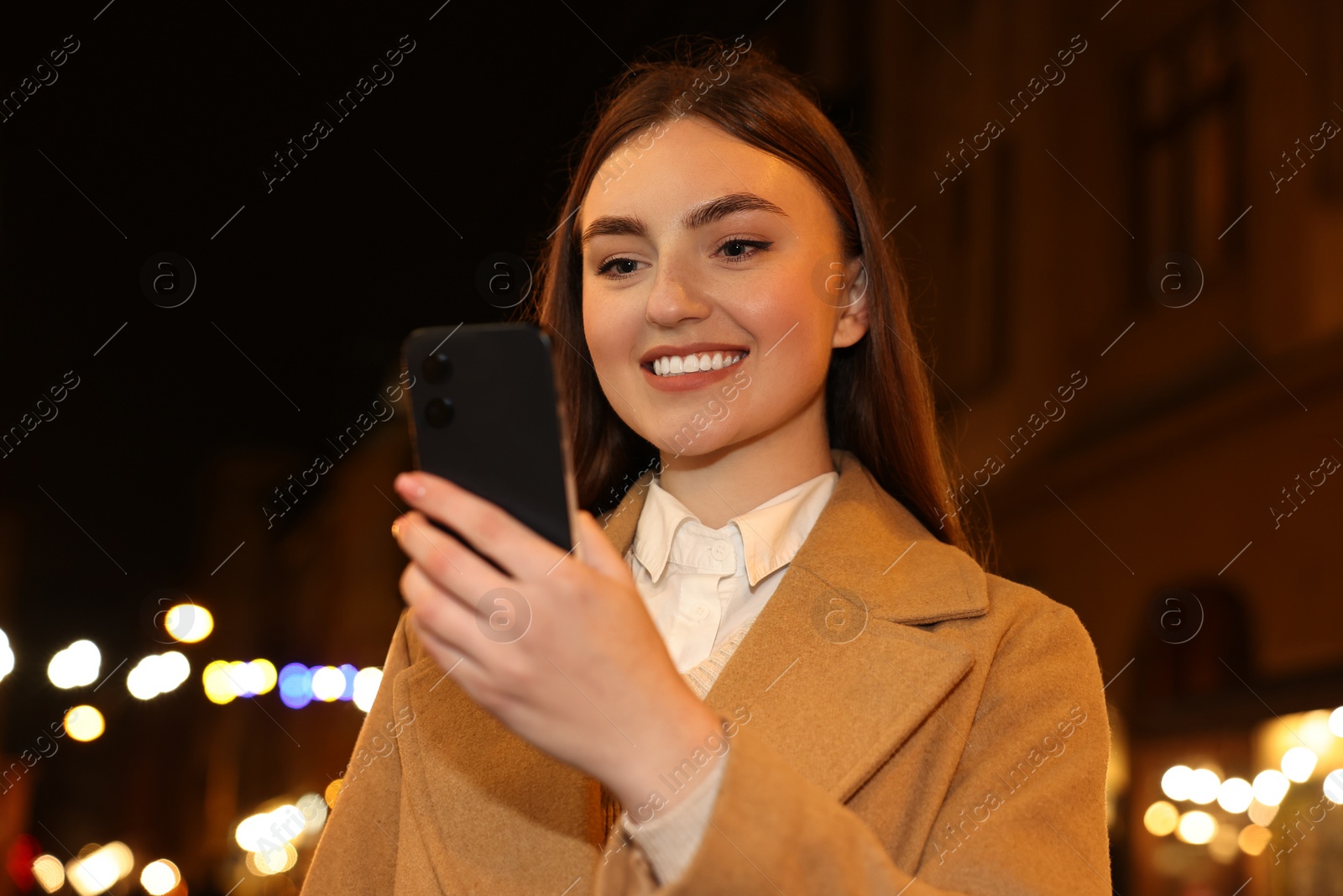 Photo of Smiling woman using smartphone on night city street