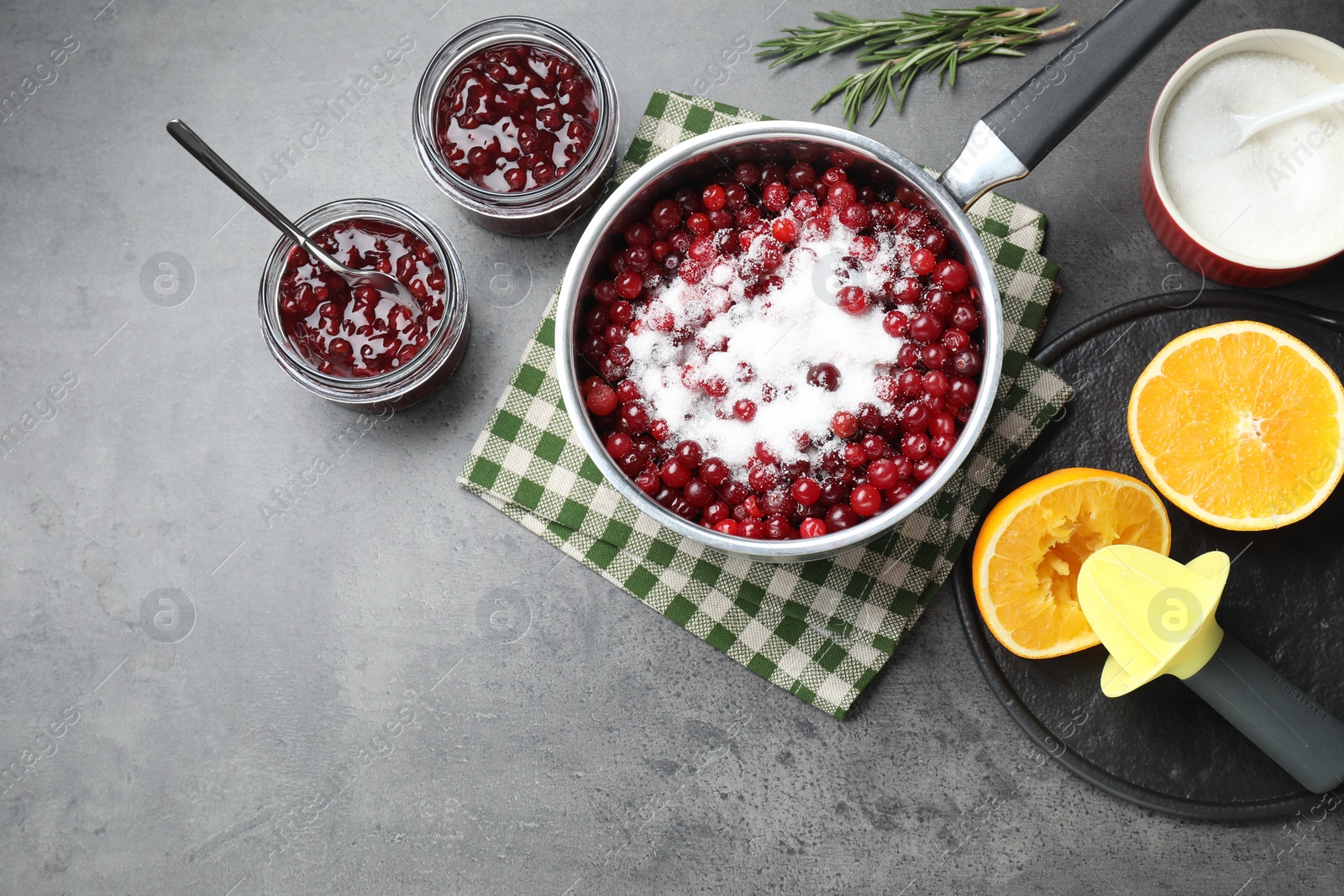 Photo of Making cranberry sauce. Fresh cranberries with sugar in saucepan and ingredients on gray table, flat lay