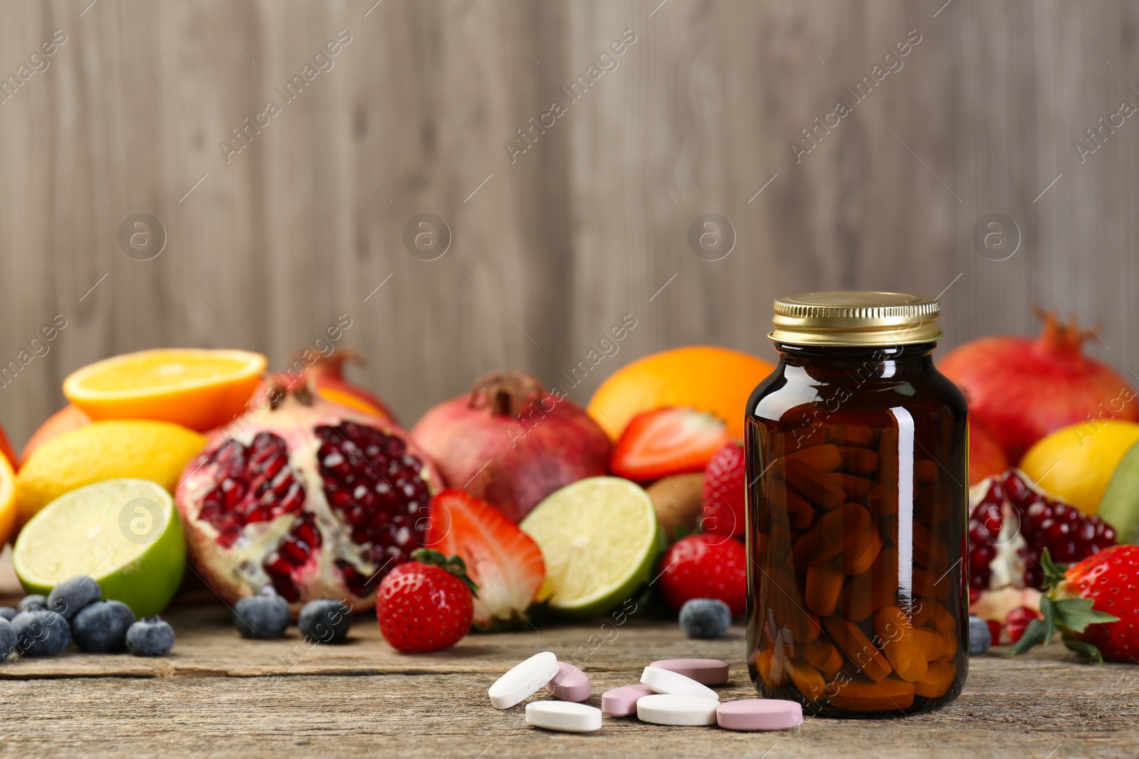 Photo of Vitamin pills, bottle and fresh fruits on wooden table. Space for text