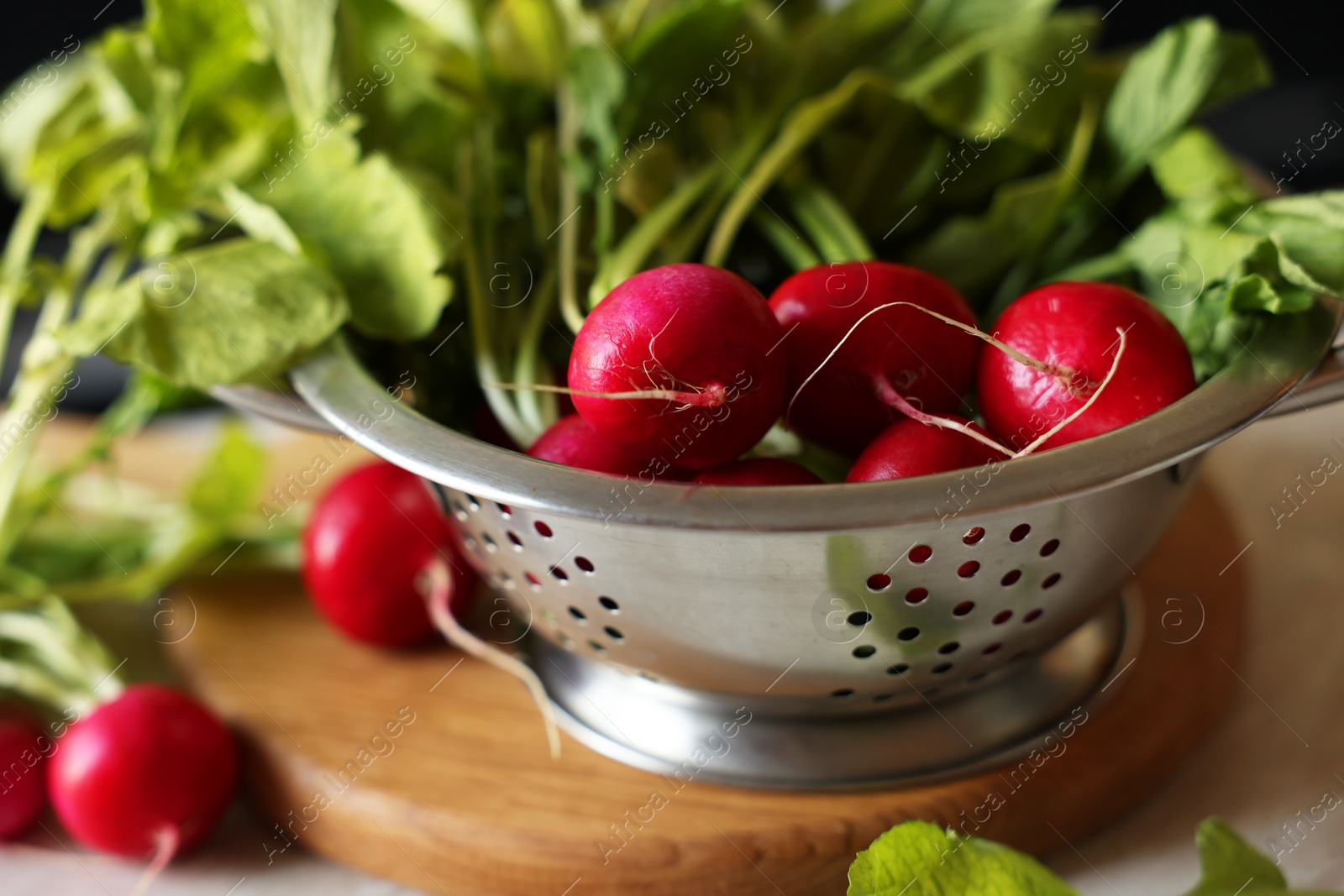 Photo of Metal colander with fresh radishes on white table, closeup