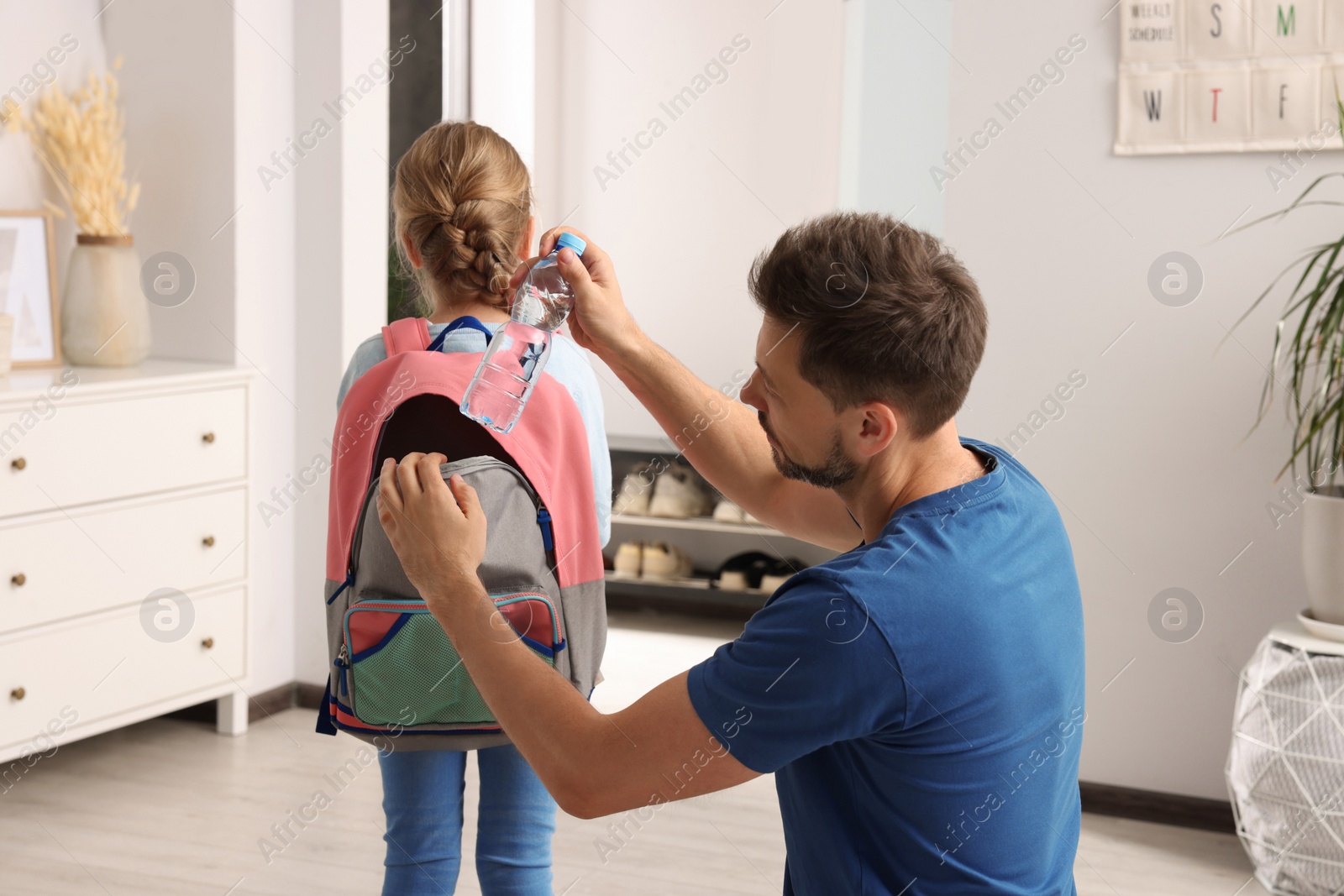 Photo of Father putting apple into daughter`s backpack at home. Preparing to school