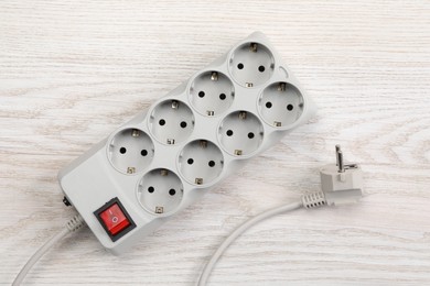 Photo of Power strip with extension cord on white wooden floor, top view. Electrician's equipment