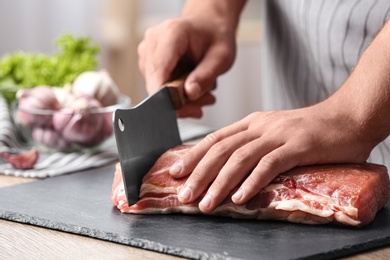 Photo of Man cutting fresh raw meat on table in kitchen, closeup