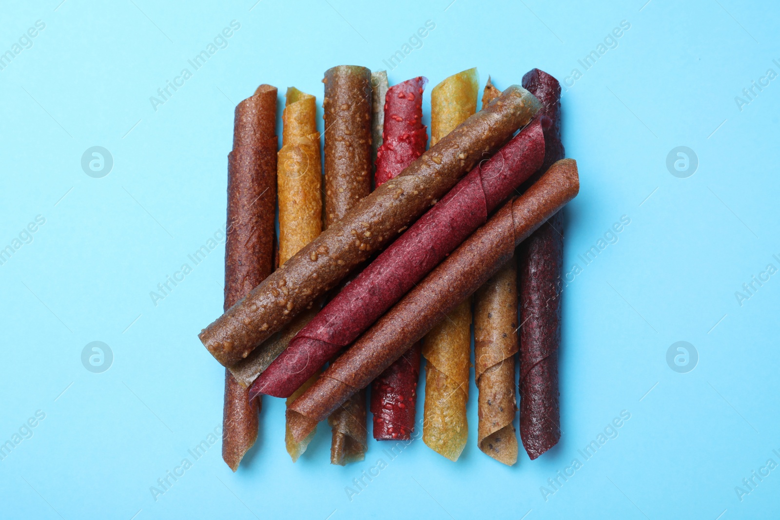 Photo of Delicious fruit leather rolls on light blue background, flat lay