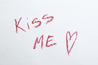 Photo of Red heart and phrase Kiss Me written with lipstick on white background, above view