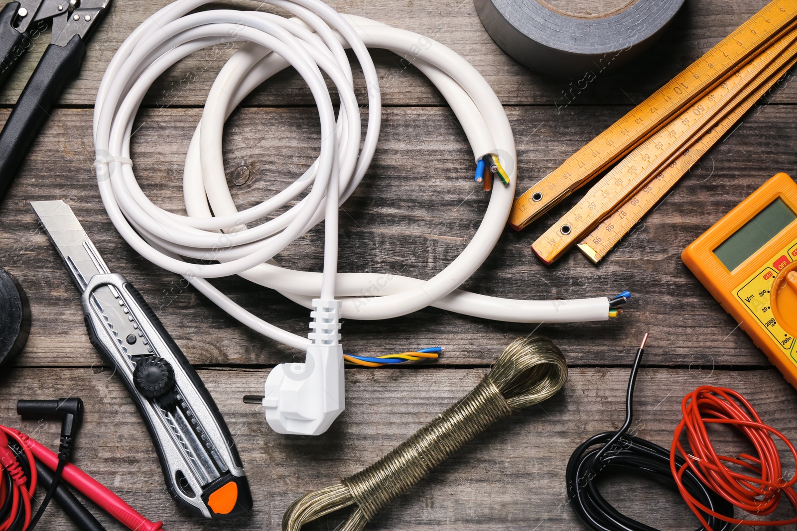 Photo of Wires and electrician's tools on wooden table, flat lay