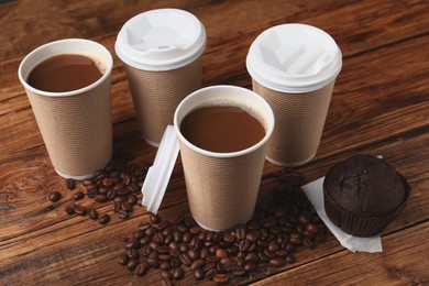 Photo of Coffee to go. Paper cups with tasty drink, muffin and beans on wooden table