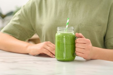 Woman with mason jar of delicious smoothie at table, closeup