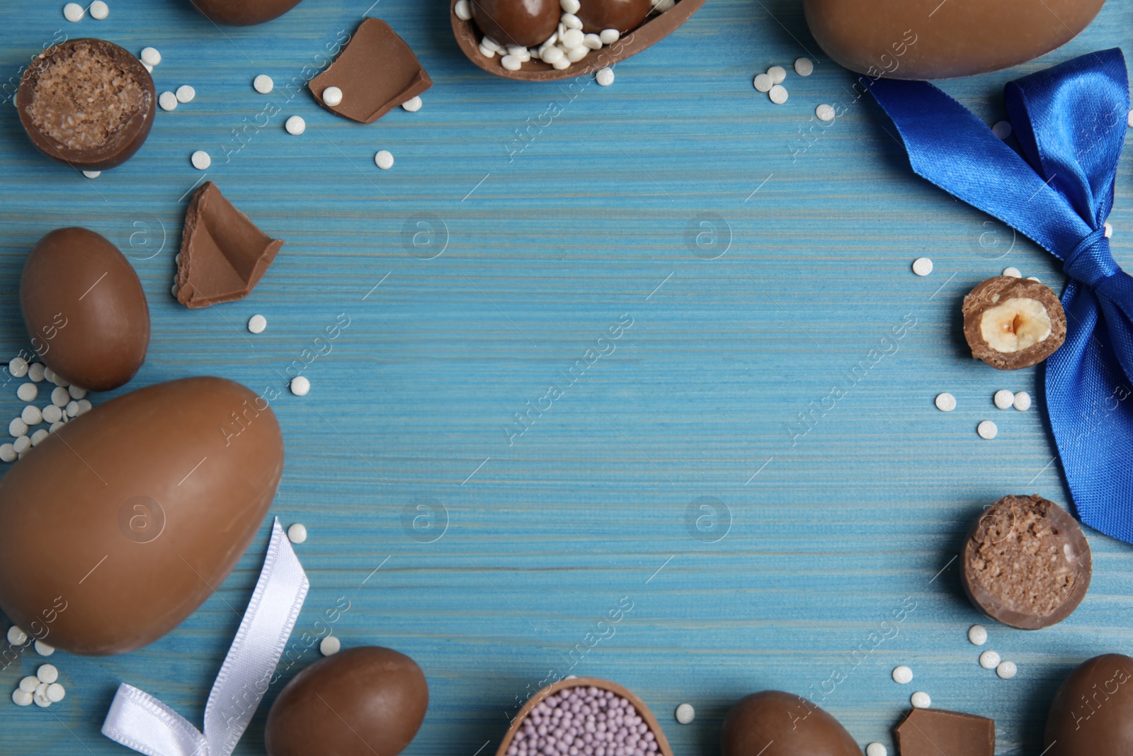 Photo of Frame of chocolate eggs and candies on blue wooden table, flat lay. Space for text