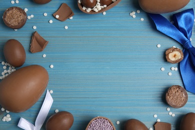 Frame of chocolate eggs and candies on blue wooden table, flat lay. Space for text