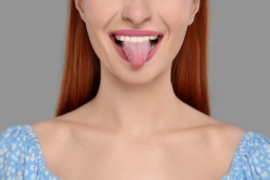 Happy woman showing her tongue on gray background, closeup