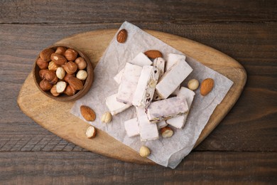 Photo of Pieces of delicious nutty nougat, hazelnuts and almonds on wooden table, top view