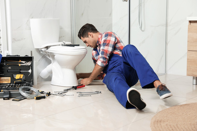 Professional plumber working with toilet bowl in bathroom