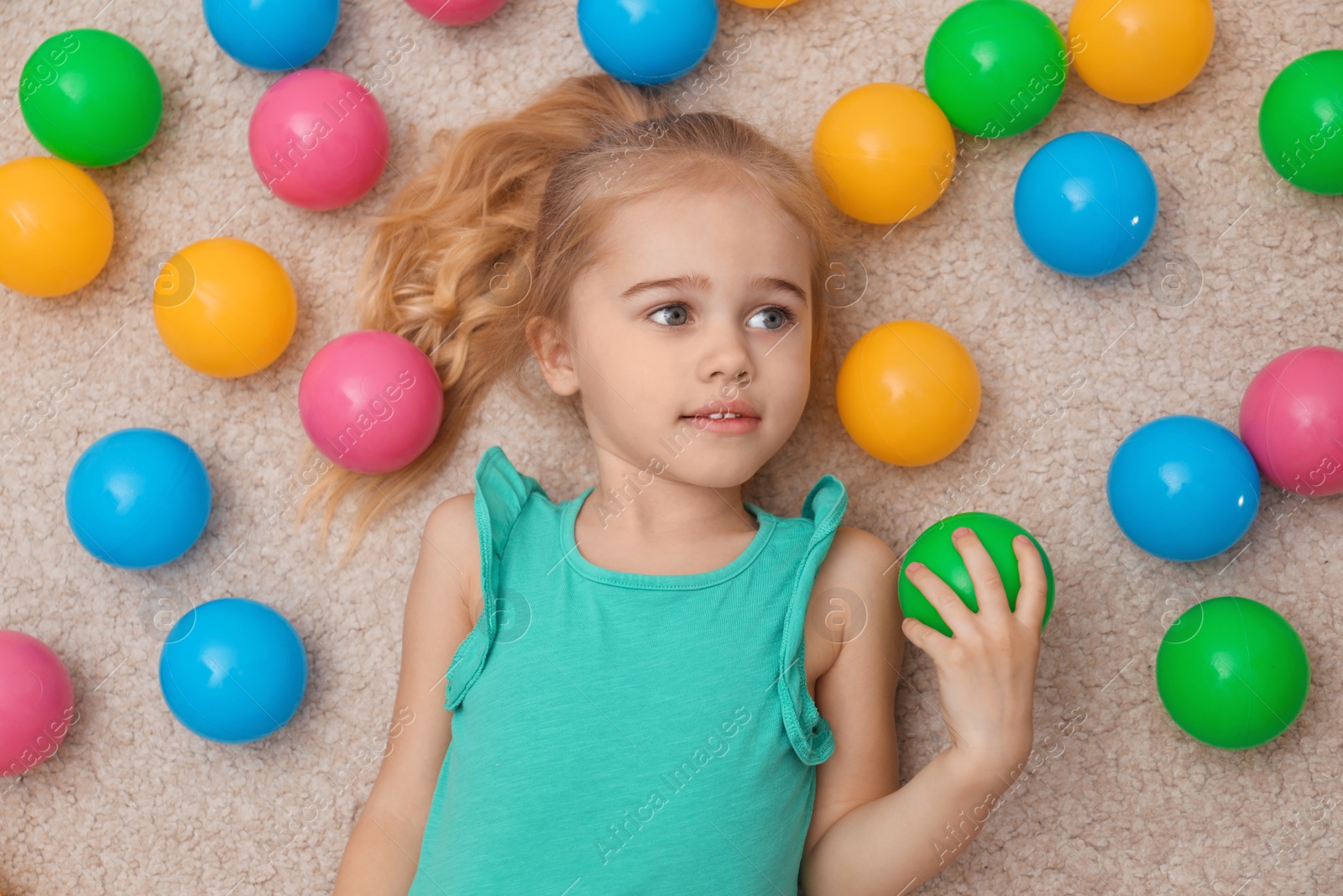 Photo of Cute little child playing with colorful balls on floor at home, top view