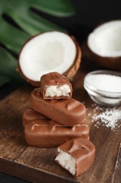 Delicious milk chocolate candy bars with coconut filling on wooden board, closeup