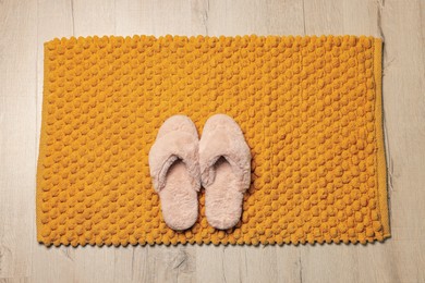 Photo of Soft orange bath mat and slippers on floor, top view