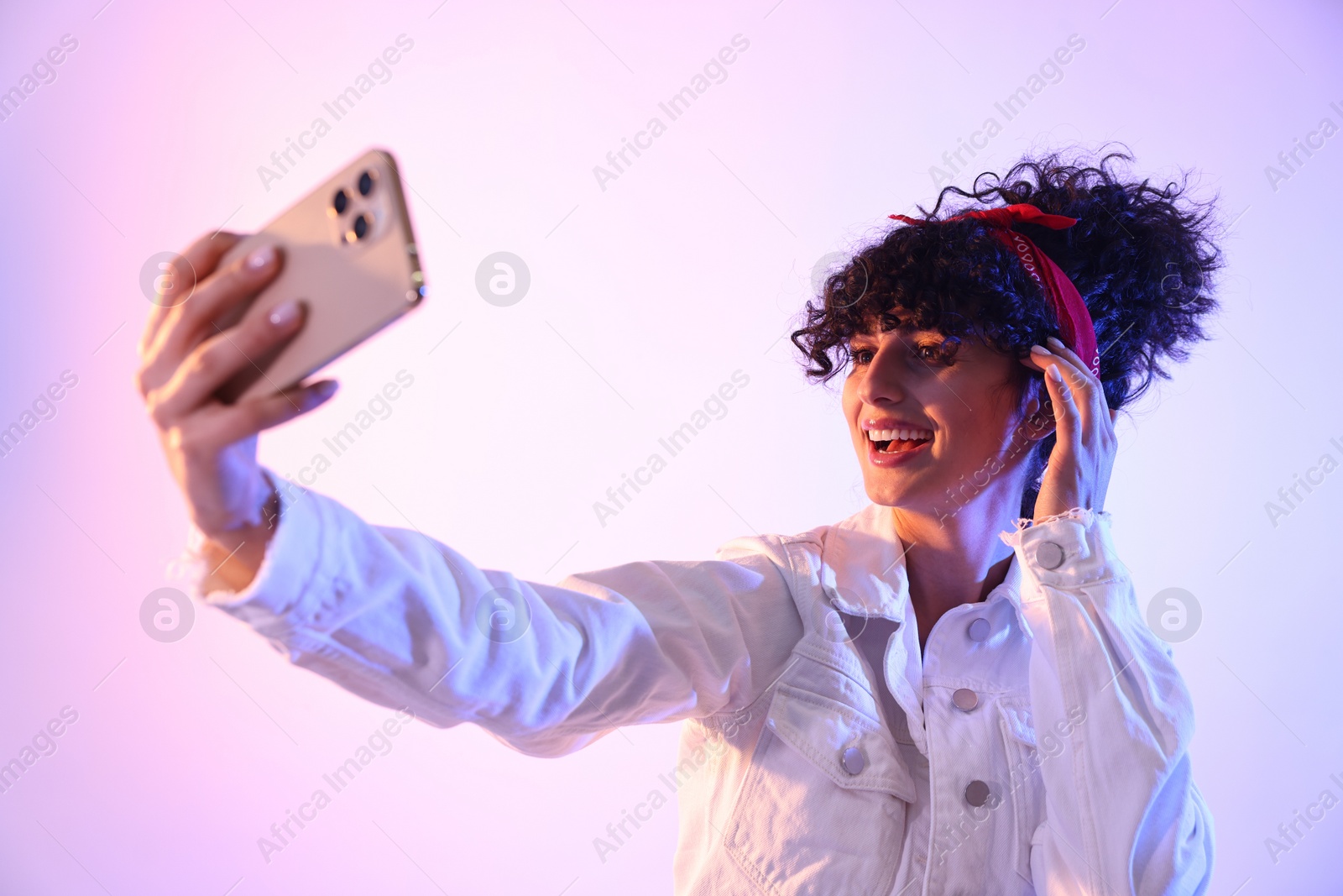 Photo of Beautiful young woman taking selfie on color background in neon lights