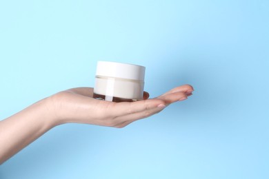 Woman holding jar of cream on light blue background, closeup