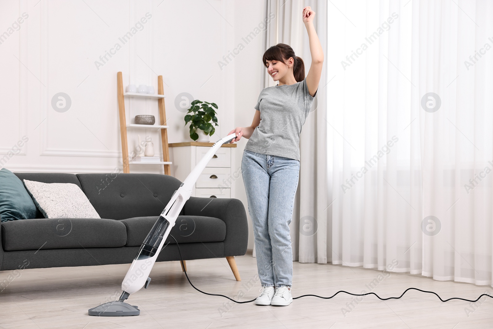 Photo of Happy young housewife cleaning floor with steam mop at home