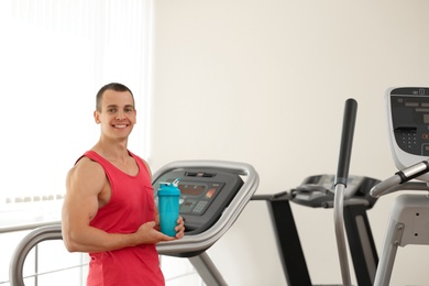 Photo of Athletic young man with protein shake on running machine in gym