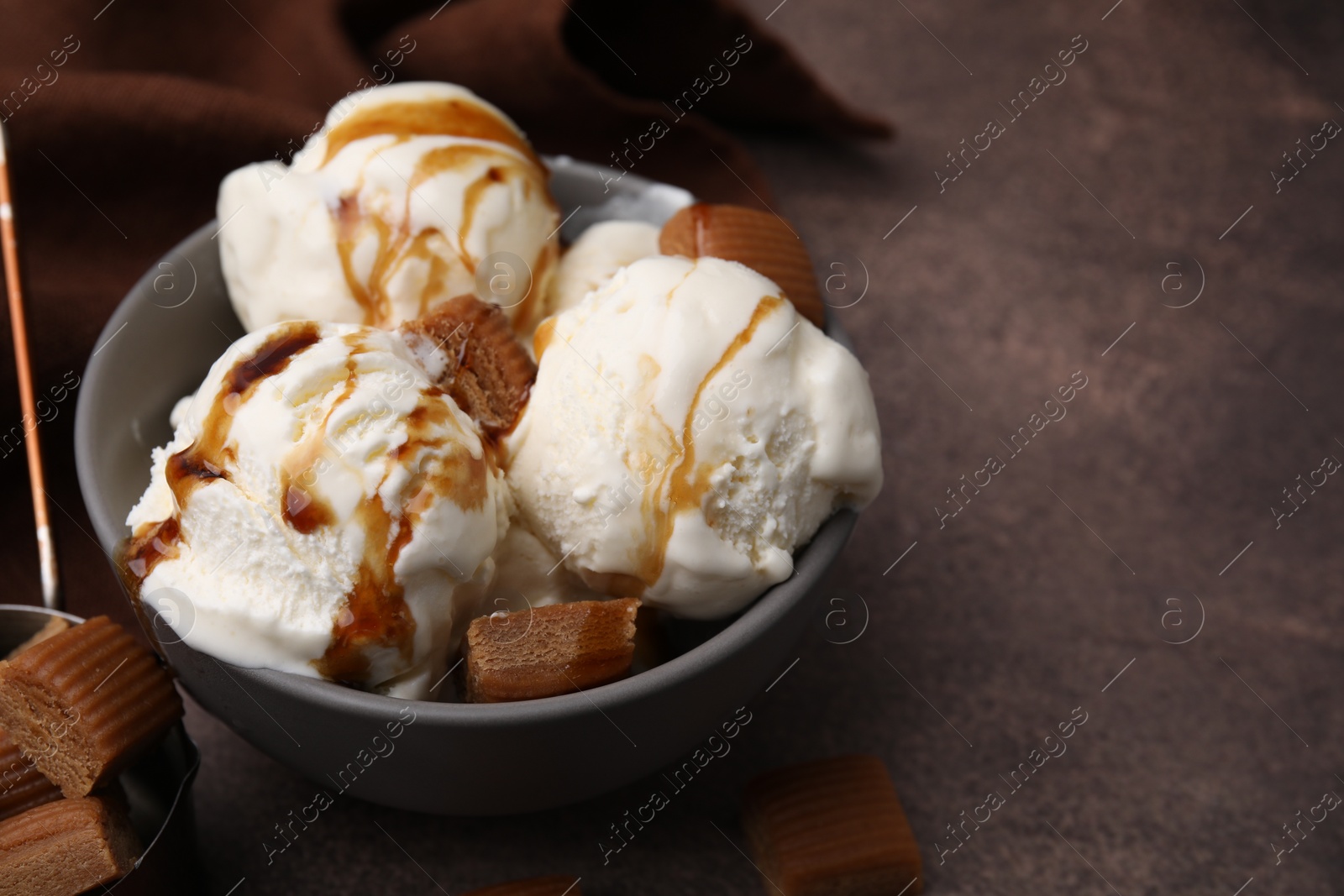 Photo of Scoops of ice cream with caramel sauce and candies on textured table, closeup. Space for text